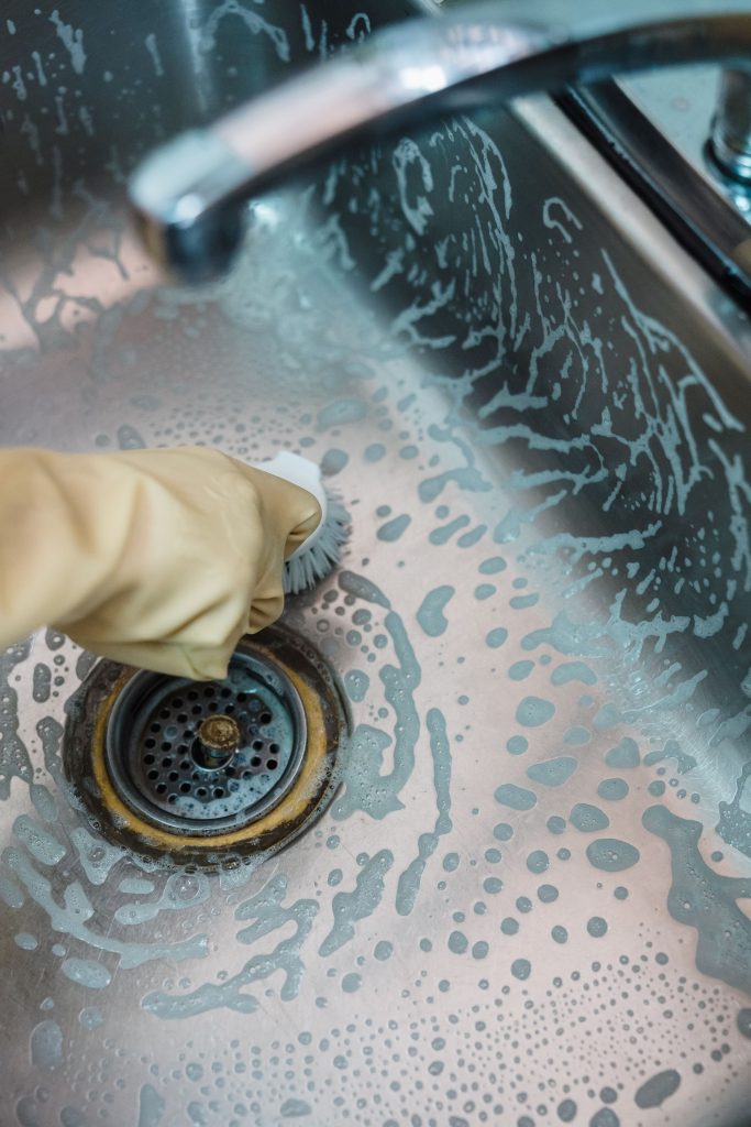Hand Wearing Glove Scrubbing Sink Drain Highlighting Drain Cleaning Services